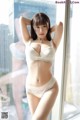 A woman in a white lingerie posing by a window.