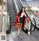 A woman in a red coat is standing on an escalator.