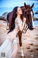 A woman in a white dress standing next to a brown horse.