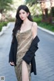 A woman in a gold dress and black blazer posing for a picture.