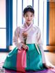 A woman in a hanbok sitting on a yoga mat holding a flower.