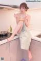 A woman in an apron is sitting on a kitchen counter.