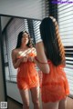 A woman in an orange lingerie looking at herself in the mirror.