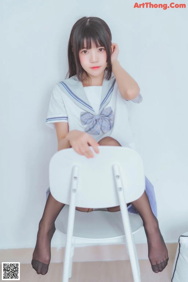 A woman in a school uniform sitting on a chair.