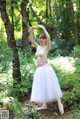 A young ballerina in a white tutu poses in the woods.