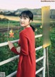 A woman in a red dress leaning against a fence.