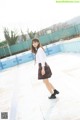 A woman in a school uniform standing in front of a swimming pool.