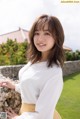 A woman leaning against a stone wall in a white shirt and yellow skirt.