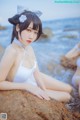 A woman in a white bathing suit sitting on a rock by the ocean.