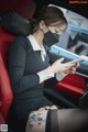 A woman wearing a face mask sitting in a car looking at her phone.