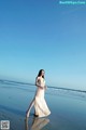 A woman in a long dress walking on the beach.