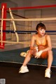 A woman in an orange bikini sitting in a boxing ring.