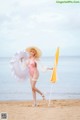 A woman in a pink bathing suit and hat holding an umbrella on the beach.