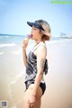 A woman in a bathing suit eating an ice cream cone on the beach.