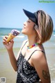 A woman in a black hat eating an ice cream cone on the beach.