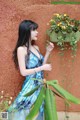 A woman in a blue dress standing next to a plant.