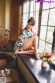 A woman sitting on a window sill next to a vase of flowers.